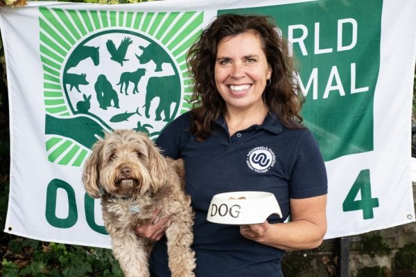 Our CEO Sarah and her dog buddy in front of a World Animal Day flag with a bowl of dog food.